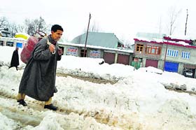 A Kashmiri carries a gas cylinder on his shoulders as he walks down a snow-covered road at Qazigund in south Kashmir's Kulgam district on Thursday
