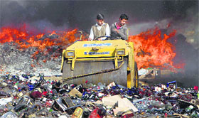 Workers operates a bulldozer to destroy seized contraband and liquor bottles next to a the burning pile of drugs and prohibited materials at a ceremony to mark the International Customs Day in Lahore on Sunday.