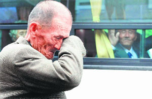 A South Korean man wipes his tears as his North Korean relative (in bus) waves to say goodbye near the border. 