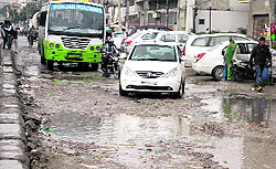 Commuters face a tough time crossing the rainwater filled potholes in Jalandhar on Saturday