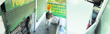 A customer peeps through the bank shutters in Ludhiana on Wednesday; and (right) an almirah ransacked by thieves.
