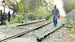 A railway gate man signals a train to pass as a broken iron bar lies near the tracks at a level crossing in Ludhiana on Sunday.