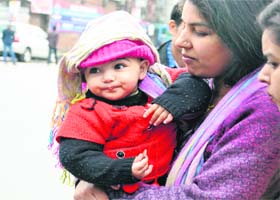 An infant is covered by his mother as rain lashed Dehradun on Thursday