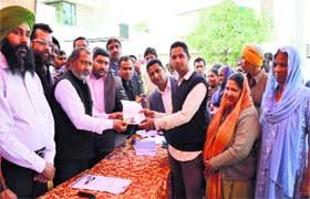 Parveen Bansal, district president of the BJP, distributes cards among beneficiaries in Ludhiana on Monday