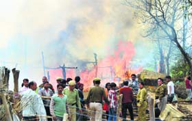 Policemen and local residents look on as fire razes thatched dwellings of migrant workers near Una on Tuesday