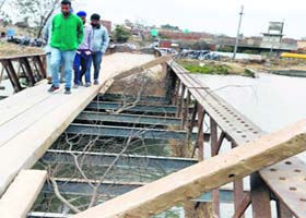 Commuters cross the damaged bridge over a canal near Tugal village