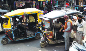 Diesel auto-rickshaws ply on a city road.
