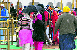 Devotees take refuge under umbrellas as sudden rainfall lashed them