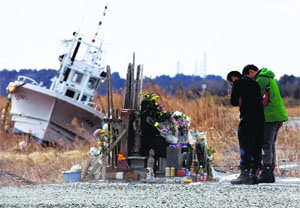 People pray for victims of the March 11, 2011 earthquake and tsunami as tsunami-crippled Fukushima Daiichi nuclear power plant is seen in the background at Namie town