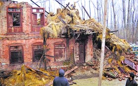 Men look at a house damaged by recent snowfall in Anantnag.