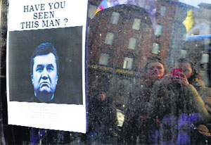 Ukrainians look at a wanted notice for fugitive Ukrainian President Victor Yanukovych, plastered on the window of a car used as barricade in Kiev's.