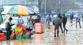 An umbrella vendor awaits customers on the roadside during rain in Srinagar on Friday.