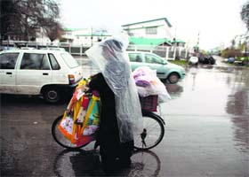 A man selling carry bags covers himself with plastic to save himself from rain in Srinagar on Sunday