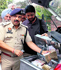 Police officials get their picture clicked while allegedly recovering cash from a UCO Bank vehicle in Jalandhar on Friday