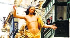 People watch from the balcony of a house as a statue of the Risen Christ is carried during an Easter Sunday procession in Cospicua, outside Valletta, Malta.