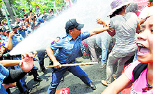 An anti-riot policeman reaches to grab a protester as they are hit with a water cannon during a protest in front of the US embassy in Manila on Wednesday