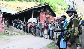 A security man stands guard as voters wait to cast their votes at Kangan village in Ganderbal district on Wednesday.