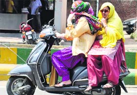 Women try to protect themselves from the heat while going on a scooter on a hot summer day in Amritsar on Sunday.