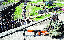A paramilitary personnel takes position atop a polling station as voters queue up outside a polling station in Kupwara district on Wednesday