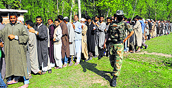 A CRPF jawan stands guard as people wait outside a polling station to cast their vote at Bakihakar Rajwar in Kupwara district on Wednesday