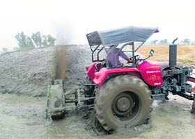 Getting innovative: A farmer plasters his stack of wheat straw with mud by a tractor-driven machine at Raonta village in Moga on Thursday