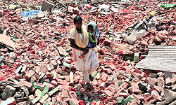 A woman, carrying her child, walks her way over the rubble
