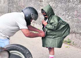Protecting the child: A father covers his daughter with a raincoat in Dehradun on Monday