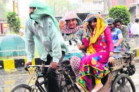 A rickshaw-puller and his passengers enjoy the heavy afternoon showers in Amritsar on Tuesday.