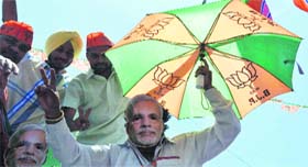 A BJP supporter wears a Modi mask and holds an umbrella with pictures of the lotus at the party office in Sector 33, Chandigarh, on Friday.