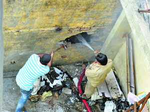 A firefighter breaks a wall of the showroom to douse fire at Chaura Bazar in Ludhiana on Sunday