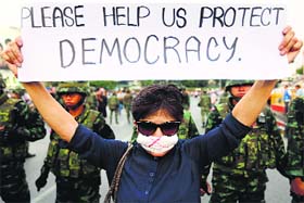A protester against military rule holds a sign in front of soldiers in Bangkok on Monday