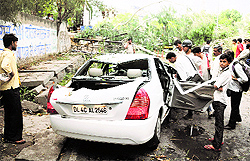 Passers-by check a car damaged by thunderstorm in New Delhi On Friday. The thunderstorm coupled with dusty winds affected road traffic, Metro services, flight operations and power supply in the city