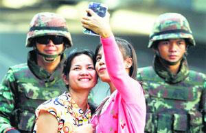 Passersby take a selfie as Thai soldiers stand guard along roads blocked around the Victory Monument in Bangkok on Friday.