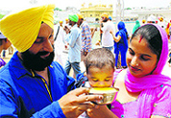 Parents offer sweet water to their child at at the Golden Temple on the occasion of the martyrdom day of Guru Arjan Dev in Amritsar on Sunday