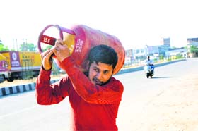 An employee of a gas agency carries a cylinder for home delivery in Jammu