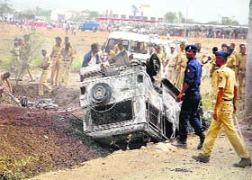 Policemen look at a vehicle torched by an irate crowd