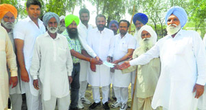 An Akali leader, along with a government employee, distributes compensation cheques to water-logging-affected farmers at Gurusar village in Muktsar district.