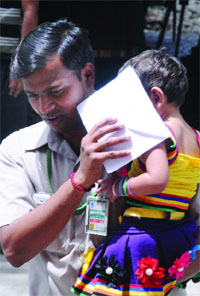 A security man covers his childs face with an invitation card to save her from the sun as the temperature rises to 45.5 C on Tuesday, at Parliament in New Delhi .