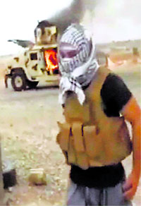 An image made from a video shows a militant standing in front of a burning Iraqi army Humvee in Tikrit.