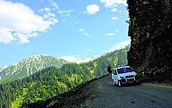 A vehicle passes on a road next to the snow-capped mountains in Sadhna Top at a height of about 11200 feet in the border area of Tangdar in Kupwara district of the Kashmir valley
