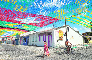 Pedestrians and a cyclist travel along a street under a canopy of national flags of countries participating in the 2014 FIFA World Cup in Porto Seguro in Brazil.