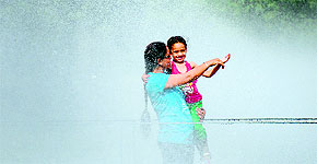 A mother-daughter duo enjoy showers from a water sprinkler on a hot Wednesday afternoon.