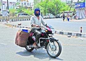 A milk vendor covers his face with a cloth and milk cans with wet jute sacks for protection from the scorching heat in Jammu