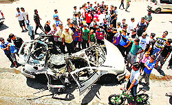 People gather around a car which was targeted in the strike on Thursday