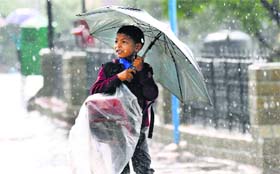 A school boy covers his school bag with a polythene sheet during rain in Shimla on Friday.