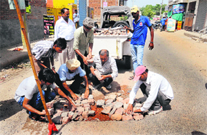 Workers of the Sahara Jan Sewa fill a pothole with bricks in Bathinda on Sunday. 
