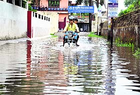 Commuters riding a motorbike wade through a waterlogged street in Dehradun on Monday