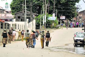 CRPF men detain a youth as protesters throw stones at them during a shutdown in Srinagar on Thursday