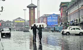 Amid the downpour: Two men take shelter under a plastic sheet during rain in Srinagar on Thursday