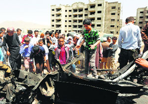 Afghans stand over the wreckage of a vehicle used in a car bomb attack at the Kabul airport on Thursday.